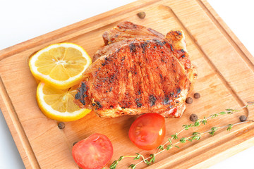 Board with cooked pork steaks on white background