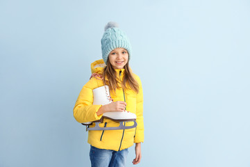 Cute little girl with ice skates on light background
