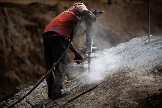 A Construction worker drills onto a rock stone at a site using a vacuum drilling machine