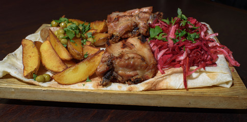 Pork ribs, rustic potato and beetroot salad on pita bread on a wooden tray. Close-up. Tasty food.