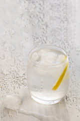 Glass of clear cold water with ice and lemon on white concrete background. Drinking water concept background