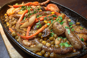 Hungarian frying pan (pork and beef sausages stewed with vegetables in dark beer) on a large wooden board. Tasty and healthy food. Close-up.