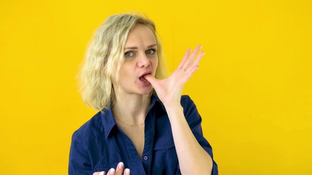 Crazy cheerful blonde girl licks fingers after tasty eating isolated on yellow studio background. Sweets. 4k footage.