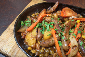 Hungarian frying pan (pork and beef sausages stewed with vegetables in dark beer) on a large wooden board. Tasty and healthy food. Close-up.