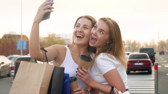 4k video of two funny smiling and laughing girls making faces while doing selfie on smartphone camera after having shopping
