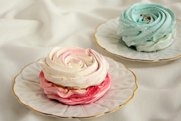 Obraz na płótnie Canvas Delicate pink and turquoise meringue cakes on saucers on a white tablecloth close up