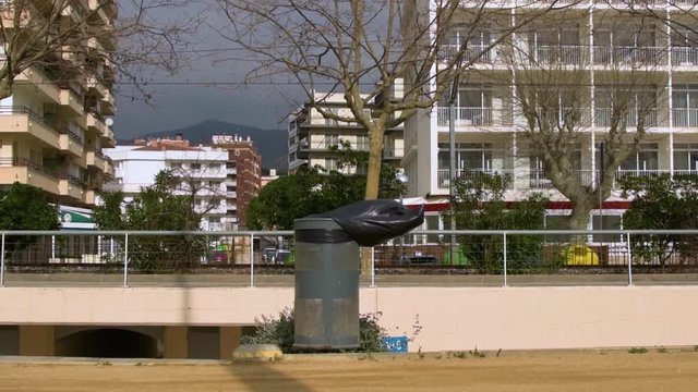 Trash bin with garbage bag moving in the wind in the street in a sunny day.