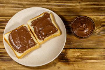 Two slices of bread with delicious chocolate hazelnut spread on wooden table. Top view