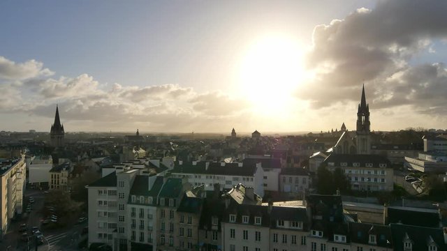 View over the rooftops of the city of Caen, a city located in Normandy, northern France. The sun is in front of the camera, there is a strong contrast. There are church steeples. Filmed in winter.