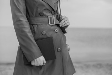 girl in a coat holds a book on a background of the sea