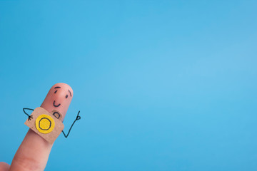 Funny finger tourist holding a camera and smiling against blue background with copy space for ad text