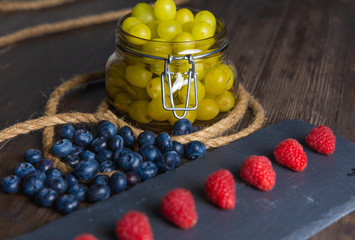 Bodegon fruit, fresh strawberries on slate plate, blueberries and glass jar with fresh grapes on an...