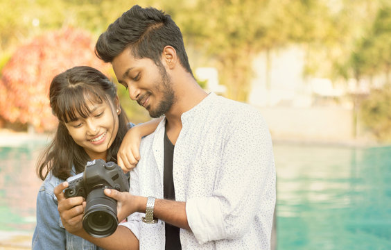 Cute Couple looking pictures on camera screen - Happy Young professional Photographer showing Images to model on his DSLR - concept of model and cameraman working together.