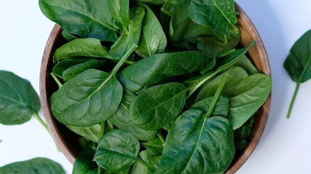 top view of spinach in a wooden bowl on white table. Close up of cooking in slow motion.