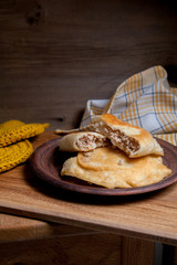 Clay plate of fried meat pies on wooden table.