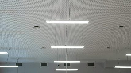 Fluorescent lights hanging from the ceiling inside the room. White walls. The lighting.