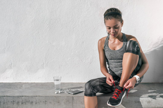 Runner woman tying running shoes laces wearing tech wearable technology smartwatch. Female athlete jogger using smart phone living a healthy active lifestyle drinking water.