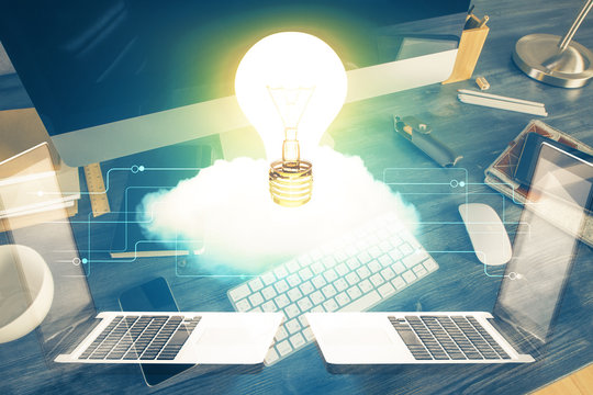 Computer on desktop in office with bulb icon hologram. Multi exposure. Concept of idea.