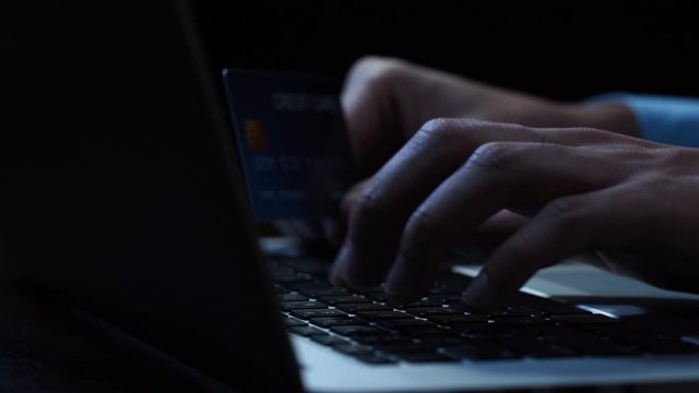 Hands of a man using laptop computer typing personal identity information making payment online with credit card at night in dark room
