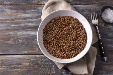 Bowl of boiled red unpolished lentils in a ceramic bowl on a wooden table