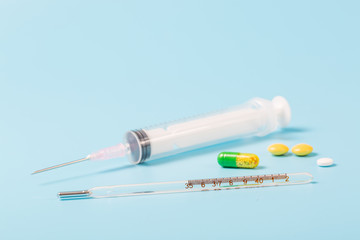 Syringe and miniature human and oral medicine and thermometer macro closeup on blue background