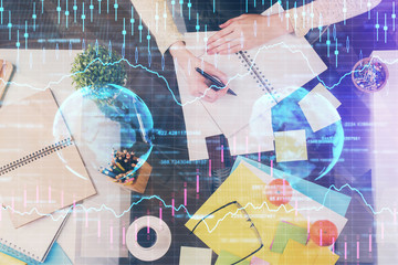 Hand taking notes in notepad. Forex chart holograms in front. Concept of research. Double exposure