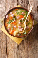 Spicy hot pea soup with potatoes, onions, carrots and ham close-up in a bowl. Vertical top view