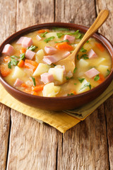 Spicy hot pea soup with potatoes, onions, carrots and ham close-up in a bowl. vertical