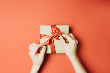 Partial view of woman tying ribbon on gift box isolated on red