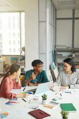 Team of designers sitting at the table with colored palette and pattern and discussing new project in team during business meeting