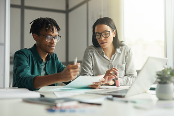 Young African businessman talknig to young businesswoman at the table at office they discussing some documents