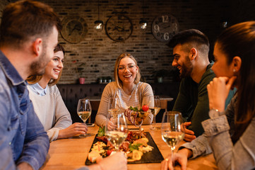 Group of young friends having fun in restaurant, talking and laughing while dining at table.