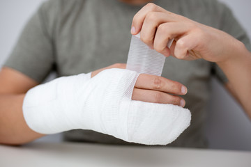 fracture and first aid concept - close up of man bandaging himself