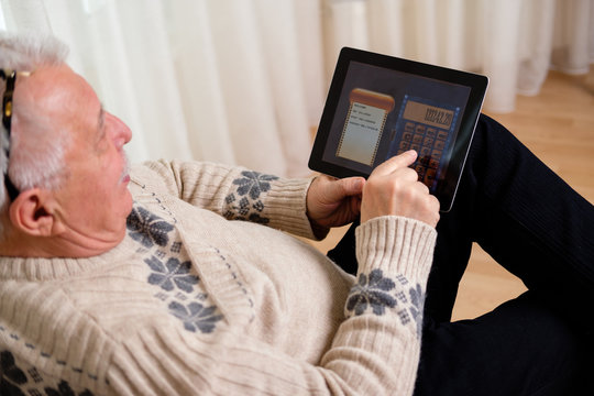 Old Man Shot From Top Sitting On A Sofa Holding A Tablet Pc And Making Calculation