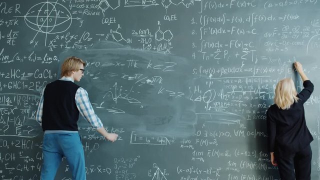 Slow motion of young man and adult woman writing formulas on blackboard in university class concentrated on science. People and lifestyle concept.