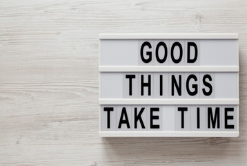 'Good things take time' words on a lightbox on a white wooden background, top view. Overhead, from above, flat lay. Space for text.