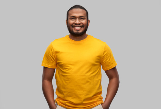 people concept - smiling young african american man in yellow t-shirt over grey background