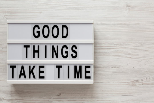 'Good things take time' words on a lightbox on a white wooden background, top view. Overhead, from above, flat lay. Copy space.