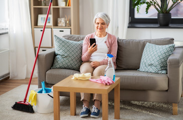 household and technology concept - happy senior woman using smartphone after cleaning home