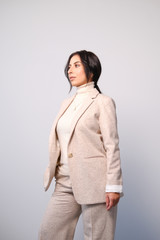 Portrait of a smiling mid-aged business woman in a light milk-colored trouser suit and turtleneck against a light wall.