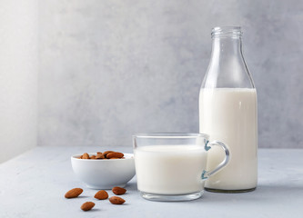 Bottle and cup of almond milk with raw almonds on a gray table. Healthy concept. Copy space.