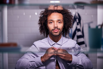 View Through Bathroom Cabinet Of Young Businessman Putting On Shirt Getting Ready For Work