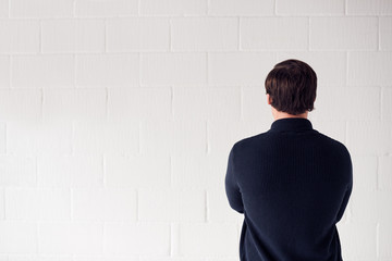 Rear View  Of Casually Dressed Man Standing Against White Studio Wall