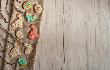 Easter composition. A border of spring willow branches with the first fluffy buds and delicious homemade cookies in the form of Easter bunnies and eggs on a light wooden background. Free space.