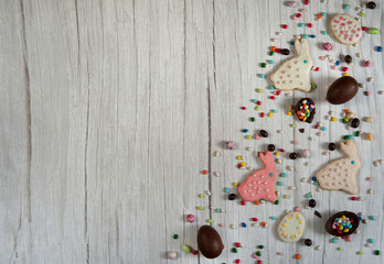 Easter composition. The border is made of homemade cookies in the form of Easter bunnies and a scattering of colored chocolate eggs on a light wooden background. Free space.