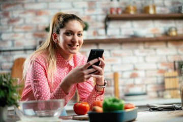 Beautiful woman in kitchen. Young woman writing message on phone. 