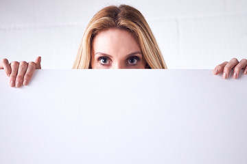 Young Woman Holding Blank White Card With Copy Space In Front Of Face Standing Against White Wall