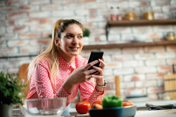 Beautiful woman in kitchen. Young woman writing message on phone. 