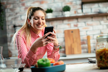 Beautiful woman in kitchen. Young woman writing message on phone. 