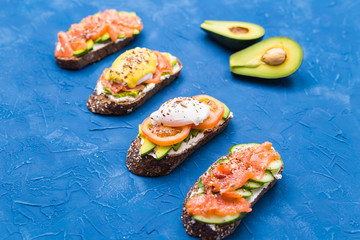 Sandwiches with smoked salmon, eggs, sauce and avocado on blue background. Concept of breakfast and healthy nutrition.